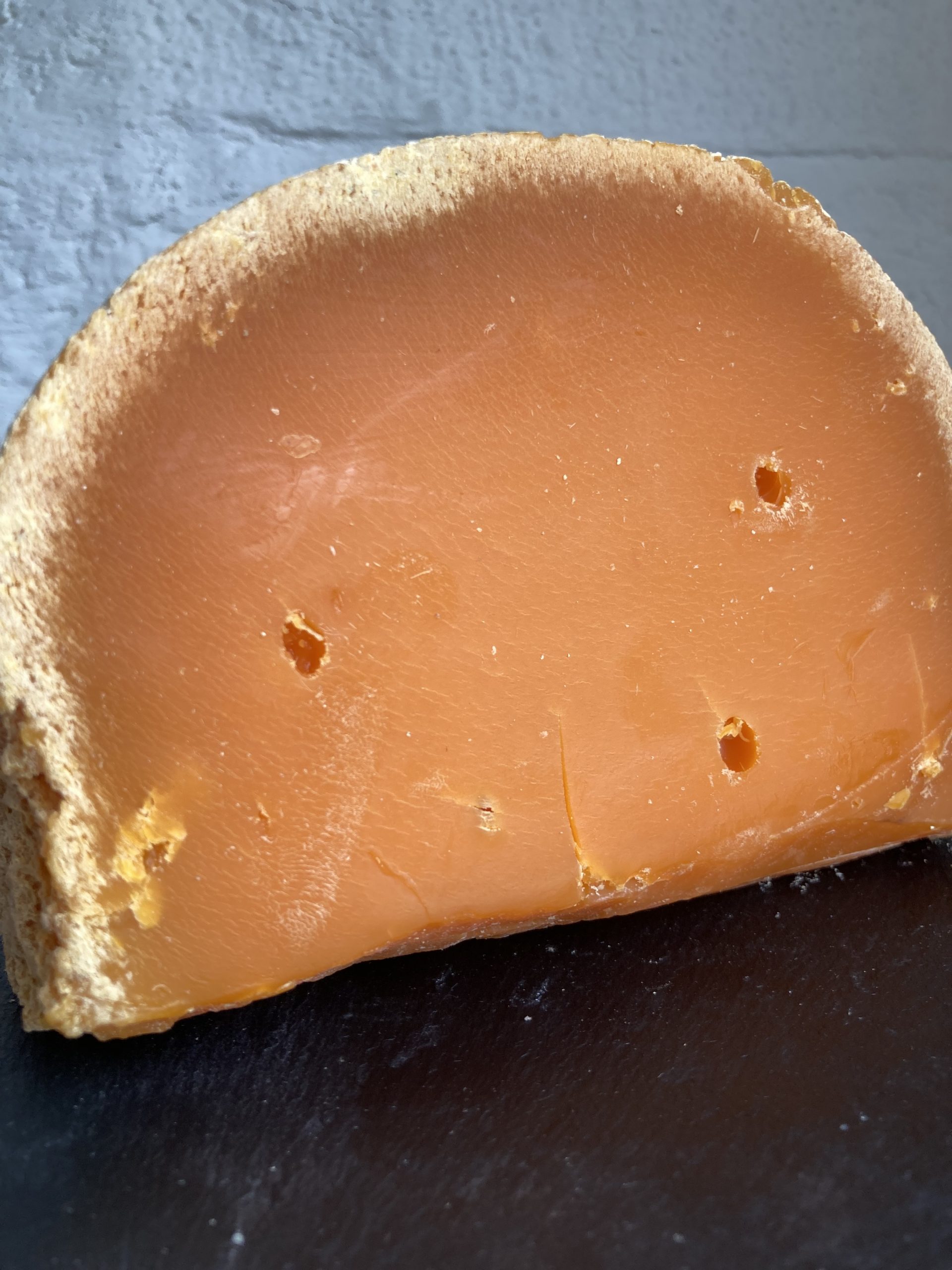 A deep orange cheese cut in circular segment of Mimolette