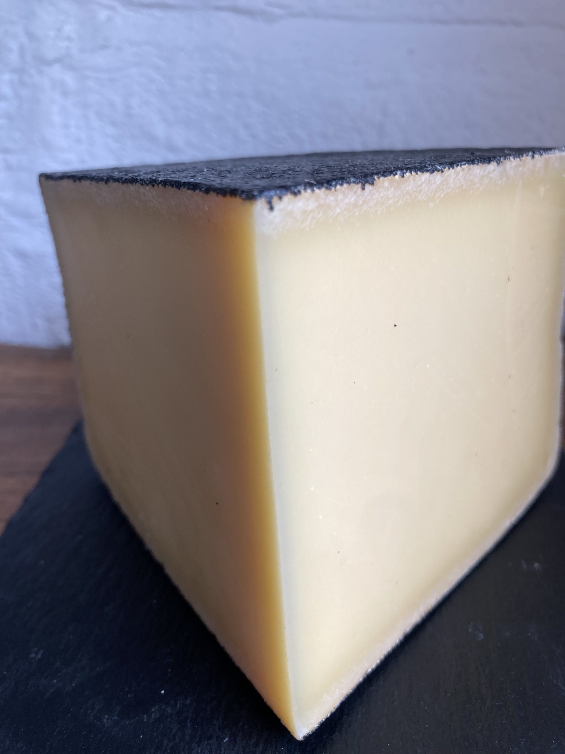 Sharp edge of a wedge of creamy coloured cheese encased in a thin black wax