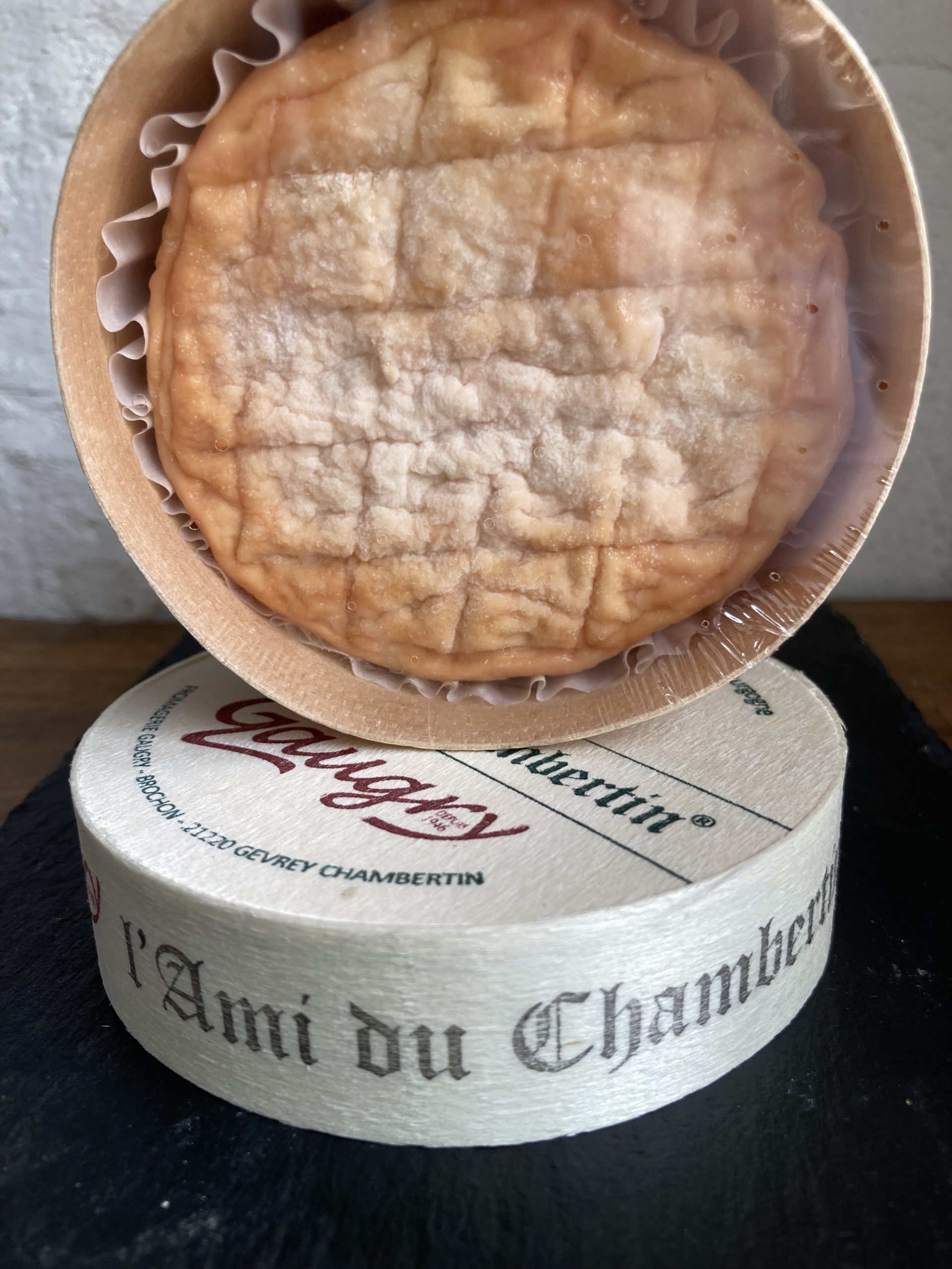 A whole small round box of orangey tinged cheese, balanced on top of its lid