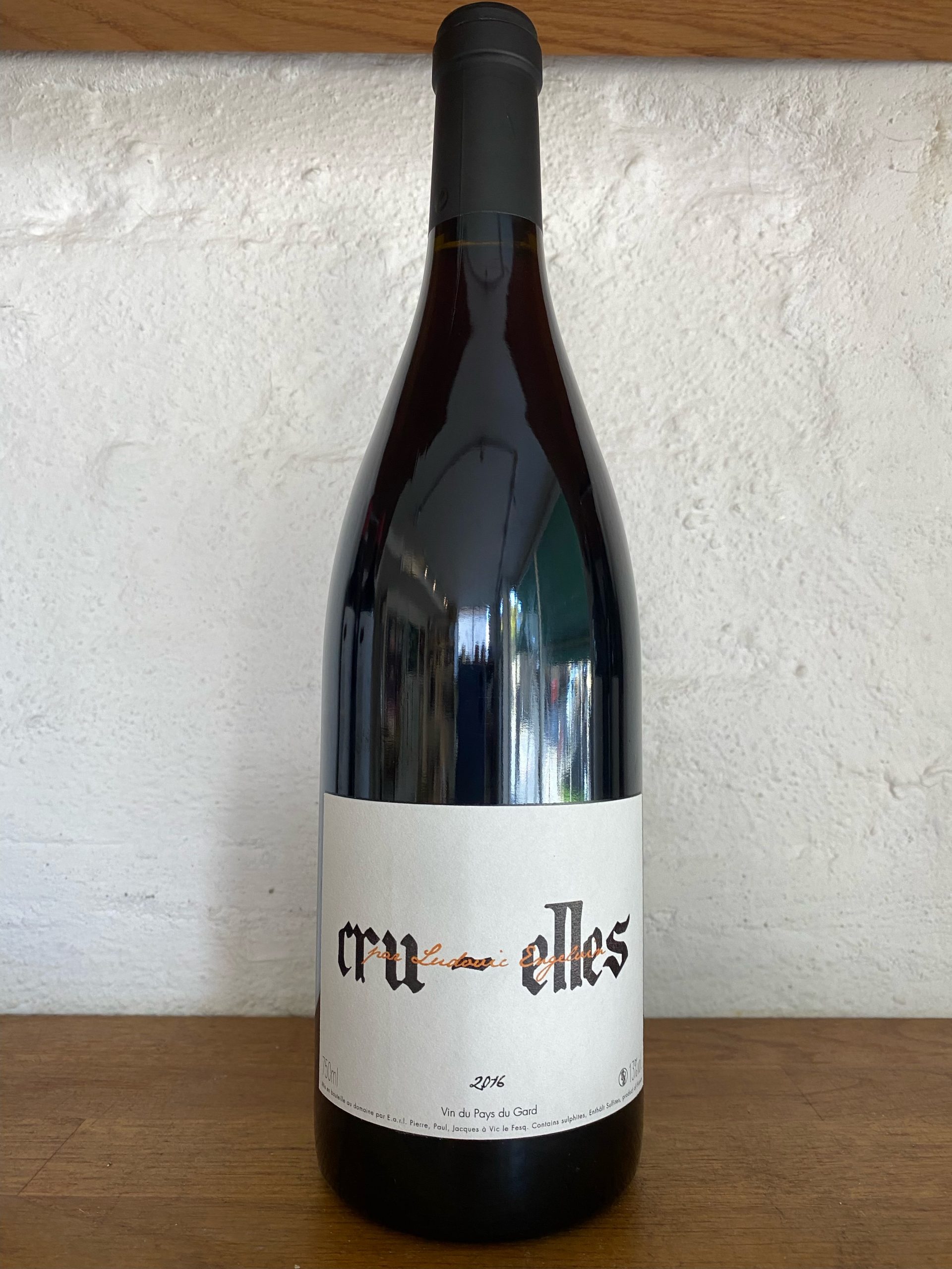 Cru Elles bottle of red wine on wooden shelf with white bricks behind